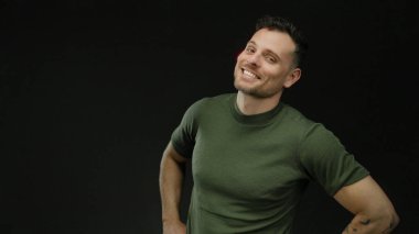 İzole edilmiş, siyah bir arkaplan, dövmeli ve yeşil gömlekli, yakışıklı ve çekici bir tavır sergileyen genç bir adam..