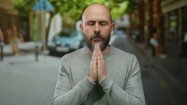 Şehrin arka planında elleri sımsıkı bağlı meditasyon yapan bir adam sakallı ve sakin bir tavır sergileyen gözleri kapalı bir şekilde şehrin atmosferinde huzur dolu bir duayı gösteriyor..