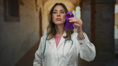 Steteskoplu İspanyol kadın doktor, eski bir üniversite koridorunda eğitim ortamında farkındalık ve desteği simgeleyen mor kurdele tutuyor..