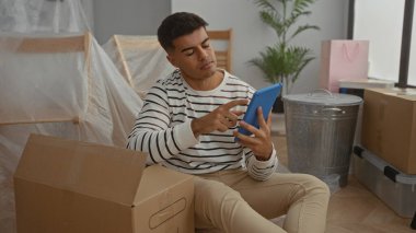 Genç adam yeni bir evde oturuyor. Etrafı kutularla çevrili. Oturma odasında, yüzünde rahat bir ifadeyle tablet kullanıyor..