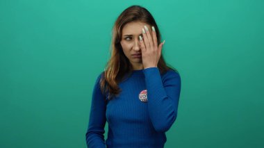 Karışık duyguları ifade eden kadın, mavi gömlekli ve oy rozetli canlı yeşil bir duvara karşı duruyor. Bu, Birleşik Devletler 'in seçim katılımını sembolize ediyor..