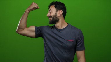 Sakallı İspanyol adam canlı yeşil bir arka plana karşı kaslarını rahatça esnetiyor..