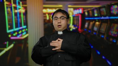 Rahip, arka planda renkli kumar makineleriyle dolu canlı bir kumarhanenin içinde şaşkın bir şekilde şaşkınlık ve endişe dolu bir ifadeyle kapalı mekan ortamını sergiliyordu..