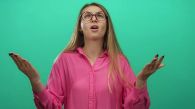 Pembe gömlekli genç bir kadın, izole edilmiş yeşil arka plan duvarına karşı anlamlı bir şekilde hareket ediyor..