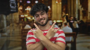 Kilisenin içinde taş jestler yapan sakallı genç adam kırmızı beyaz çizgili gömlek giyiyor. Mutluluk kutlaması içeride İspanyol kökenli..