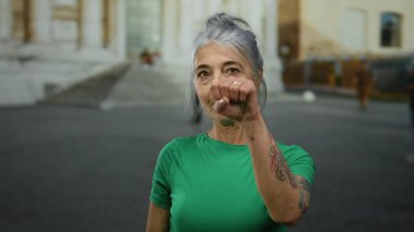 Şehir caddesinde yeşil tişörtlü, kır saçlı yaşlı bir kadın, ilginç bir yüz ifadesiyle, şehir merkezinin ortasında ilginç bir şekilde gezen biri..