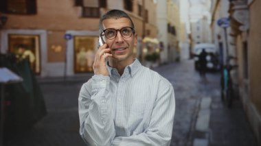 Güneşli bir Avrupa caddesinde akıllı telefon kullanan bir adam, günlük kıyafetlerini giymiş bir şehir ortamında bağlantı kuruyor..