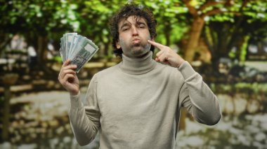 Canlı bir park ortamında bangladeshi taka 'yı elinde tutan İspanyol bir adam, açık hava sahnesini kayda değer bir şekilde sergiliyor..
