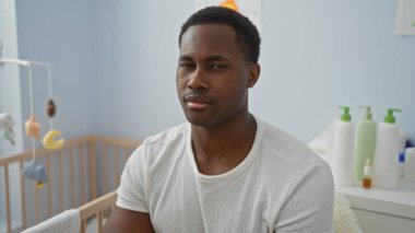 Genç adam güvenli bir şekilde bir yatak odasında beşiğin yanında oturur, evin içinde huzurlu bir aile ortamı sergiler..