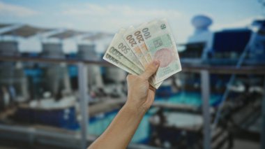 Kafkasyalı bir adam, elinde Czech Koruna banknotları olan bir deniz gezisi teknesinde, seyahat ve para birimlerine odaklı bir açık hava ortamındaki finansal işlemleri gösteriyor..