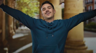 Mavi kapüşonlu genç İspanyol adam şehir meydanında emniyet kemerlerinin altında rahat bir ifadeyle esniyor..