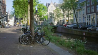 Bulanık amfi kanal arkaplanı olan bir ağaca yaslanmış bisikletler, dağılmış sokak sahnelerini, yemyeşil ağaçları ve huzurlu su yolu boyunca geleneksel evleri yakalıyor..