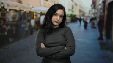 Çapraz kolları olan bir kadın sokak gösterisinde kendine güveni ve esmer saçlarıyla şehir hayatını sergiliyor..