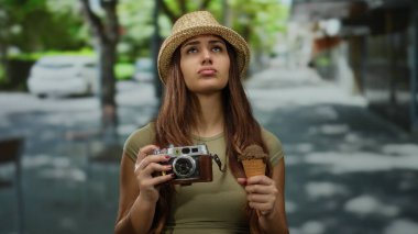 Güneşli caddede elinde kamera ve dondurma tutan bir kadın bir şehir keşfi anı yakalıyor..