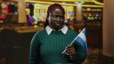 Kumarhane ortamında salvador bayrağı taşıyan kadının etrafı kültürel çeşitliliği yansıtan canlı kumar makineleriyle çevrili.