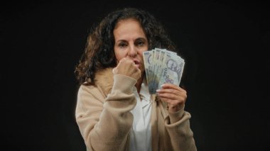 Romen banknotlarını elinde tutan orta yaşlı bir kadın, izole edilmiş bir siyah arka plana karşı, mali güç ve kararlı bir ifadeyle gücü sembolize ediyor..