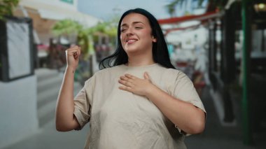 Kentsel sokak ortamında güven içinde gülümseyen bir kadın açık hava ortamında iyimserlik ve kendine güvenin olduğunu gösteriyor..