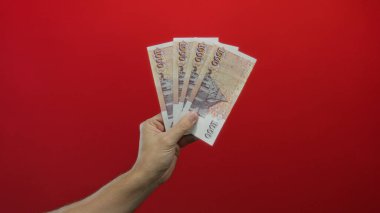 İzlanda banknotları elinde tutan adam canlı kırmızı arka plan, finansal kavramları ve para biriminin odak noktasını gösteriyor.