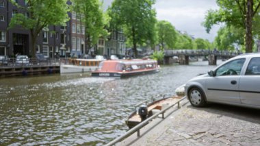 Güneşli bir gökyüzünün altında ikonik mimari sergilenen Amfitik su yolu boyunca bulanık tekne ve araba manzaralı kanal manzarası.