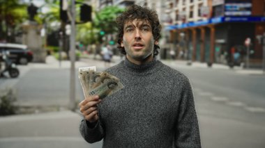 Bir şehir caddesinde elinde İngiltere sterlini tutan bir adam süveter giyiyor, finansal başarı ve kentsel yaşam enerjisini iletiyor..