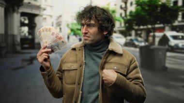 Şehir caddesinde elinde Türk lirası banknotları tutan İspanyol bir adam, şehir yaşamını ve döviz kurunu açık arka planda odaklı bir ifadeyle gösteriyor..