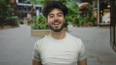 Kentsel sokak ortamında sakallı genç adam, günlük beyaz gömlekler giyiyor olumlu duygular ve bulanık şehir geçmişine karşı gevşek davranışlar sergiliyor.