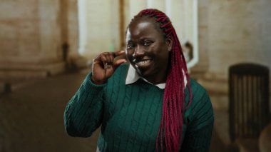 Eski üniversitede küçük beden giyinen, gülümseyen, pembe örgülü, yeşil kazaklı, hayat dolu, akademik atmosferi yakalayan bir kadın..