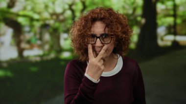 Parkta, gözlüklü, açık havada kıvırcık saçlı, ciddi ifadeli ve güneşli gökyüzünün altında gündelik giysiler giyen kadınlar..