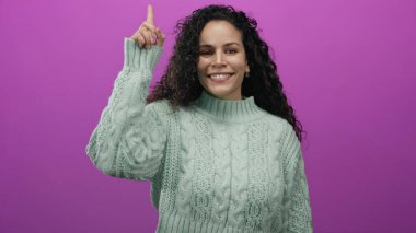 Naneli süveter giyen bir kadın canlı pembe bir duvara işaret ediyor. Tecrit edilmiş bir stüdyo ortamında gençlik hisleriyle neşe ve pozitifliği ifade ediyor..