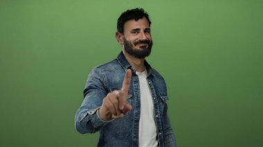 Sakallı İspanyol adam yeşil arka planda parmak hareketi yapmıyor..