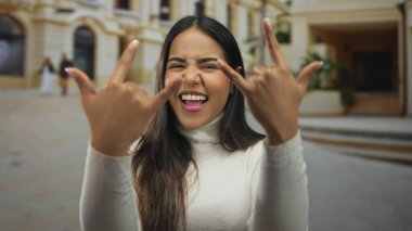 Kadın bir sokak sahnesini sallamak için ellerini kaldırıyor. Latin bir İspanyol figürü açık havada poz veriyor, boynuzlarıyla gülümsüyor ve hareketli bir ifade yaratıyor..