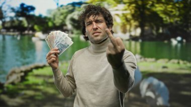 Parkta İspanyol bir adam elinde Polonya parası, orta parmağını gösteriyor ve açık havada, güneşli bir günde öfkesini gösteriyor..