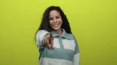 İzole edilmiş sarı arka planda gülümseyen, kıvırcık saçlı, çizgili süveter giyen, arkadaş canlısı bir ifade sergileyen bir kadın..