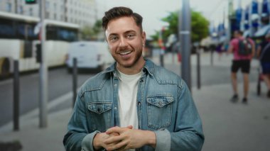 Kot ceketli genç adam arka planda otobüsler ve yayalar ile işlek şehir caddesinde duruyor, şehir dışı yaşam tarzını sergiliyor..