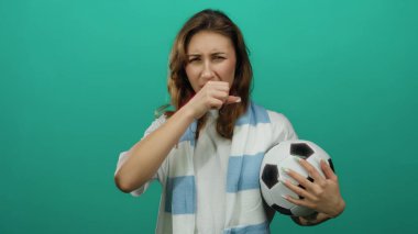 Yeşil duvara karşı mavi eşarp takan kadın izole bir ortamda duygularını ifade ediyor. Kendine güvenen genç ve oyuncu bir hayran coşkusu sergiliyor..