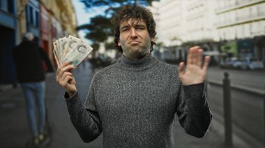 Şehirde İspanyol bir adam elinde İngiliz sterliniyle dolup taşıyor. İşlek caddelerde para konusunda temkinli davrandığını söylüyor..