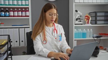 Modern bir klinikte, tibbi aletler ve canlı kimyasallarla çevrili bir dizüstü bilgisayar üzerinde çalışan kadın doktor profesyonelliği ve dikkati örnek alıyor..