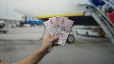 Terminal 1 'deki bir havaalanının yanında elinde Türk lirası tutan adam, seyahat ve finans konularını dinamik bir ortamda yakalıyor..