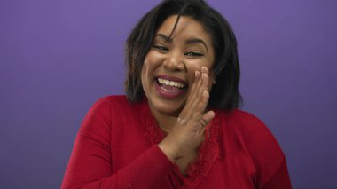Neşeli bir şekilde gülümseyen kadın canlı bir mor arka plana karşı gizli bir paylaşım jesti yapar, neşe ve entrika yayar..
