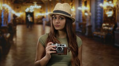 Müzede elinde antika bir kamerayla gezen, etrafı sanat ve zarif dekorlarla çevrili genç bir İspanyol kadın, kapalı bir turist deneyimi yaratıyor..