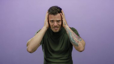 Mor arka planda dövmesi olan genç bir adam ellerini modern izole bir ortamda kullanarak duygularını ifade ederken şaşkın görünüyor..