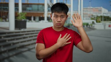 Bir sokak ortasında şehir merkezinde duran genç Çinli bir adam. Bir eli göğsünde, diğeri ise modern mimarinin önünde yükselen kırmızı bir gömlek giyiyor..