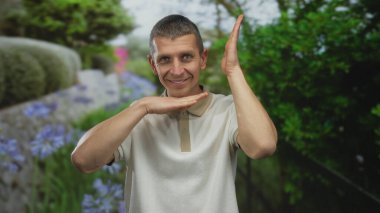 Parktaki beyaz adam, güneşli bir günde yemyeşil ve canlı çiçeklerin arasında enerjik bir şekilde hareketler yapar, neşe saçar ve doğayla bağlantı kurar..