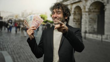 İspanyol adam kameraya gülümseyip işaret ederken kalabalık bir sokak manzarasında elinde Tayland banknotları tutuyordu..