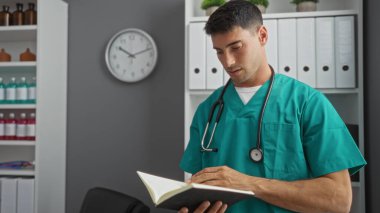 Klinikte ameliyat önlüğü ve steteskop giyen genç bir adam, kapalı bir hastane odasında, çekici bir portre ortamında çekilmiş profesyonel ve odaklanmış bir ifadeyle notları inceliyor.