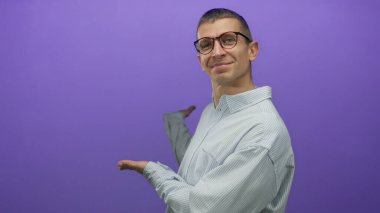 Gözlüklü bir adam mor bir arkaplanı işaret ediyor, izole edilmiş ve gülümseyen, konsept ya da fikir sunan, kendine güvenen bir duruşu olan çizgili gömlek giyen, profesyonel tavır sergiliyor..