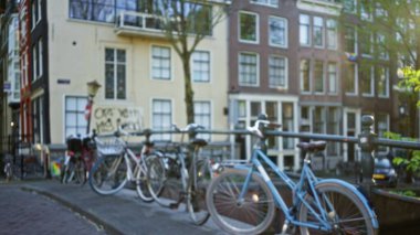Hollanda, Amsterdam 'da bir kanal boyunca park etmiş bisikletlerin odaksız görüntüsü, bulanık arkaplandaki ikonik Hollanda mimarisini vurgulayan bir bokeh etkisi ile.