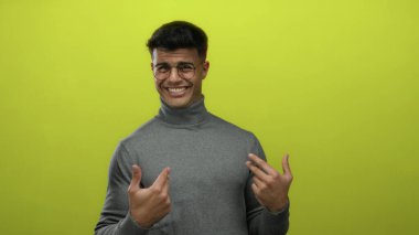 Gri balıkçı yakalı genç adam canlı sarı bir arka plana karşı gülerek neşe ve modern tarzını sergiliyor..