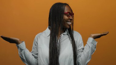 Kıvırcık saçlı, turuncu duvarın arkasında gülümseyen neşeli ve anlamlı pozlar veren bir kadın..