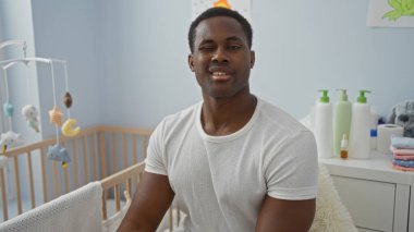 Bebek beşiğinin yanında, yatak odasında oturan yakışıklı bir adam, yumuşak ışıklandırmayla çevrili, sıcak, rahatlatıcı bir atmosfer veren, aile, ev ya da ebeveynlik teması için mükemmel..